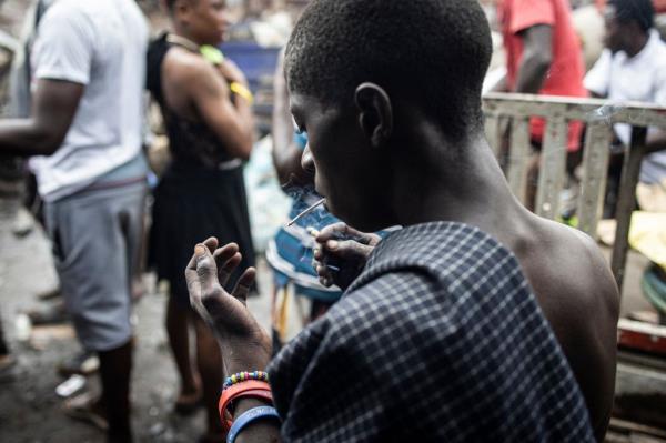 Photo of a young man smoking Kush and staring at his hand in a drug den at the Kington landfill site in Freetown, Sierra Leone
